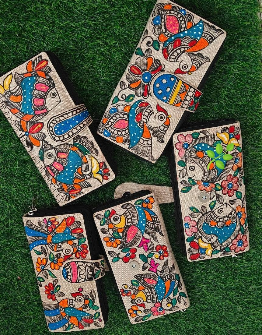 Five Madhubani painted jute clutches displayed on grass